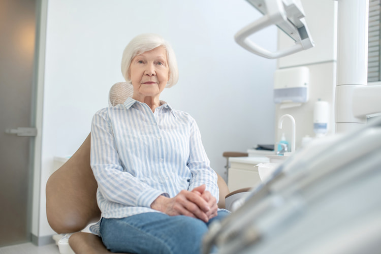 an old woman is sitting on a dental chair waiting for her CDCP-covered dental treatment.