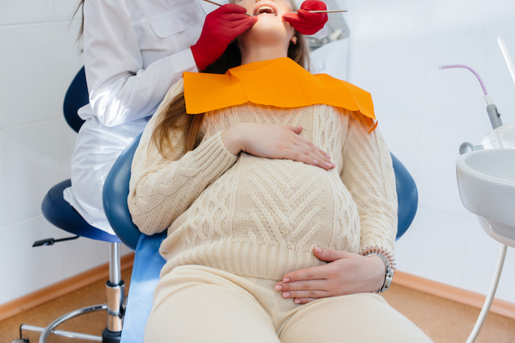A dentist is treating and examining the oral cavity of a pregnant woman in a dental office.