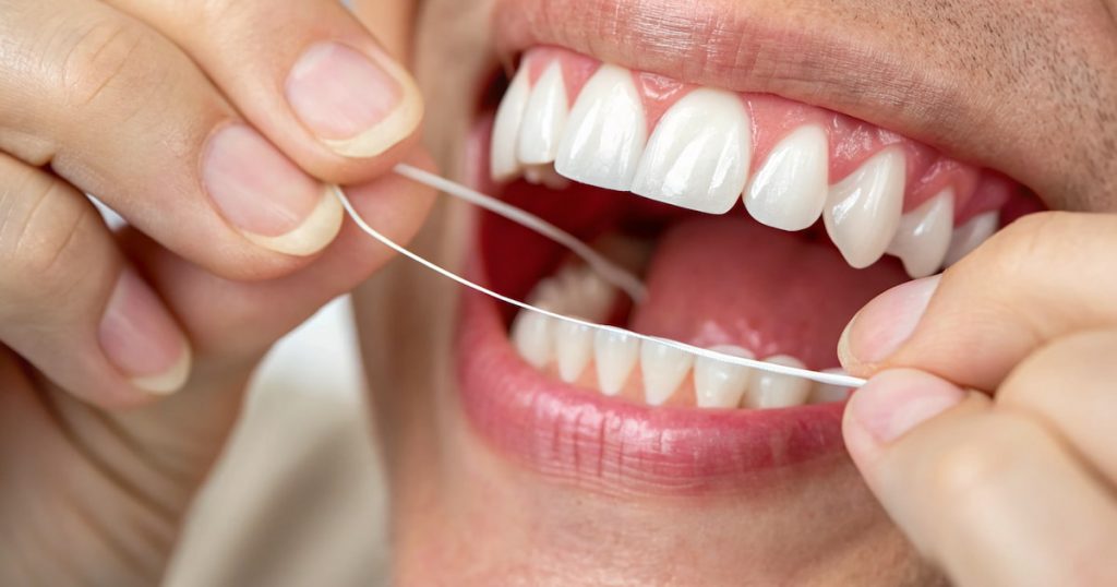 Close-up of hands gently flossing between teeth to avoid gums bleed while flossing