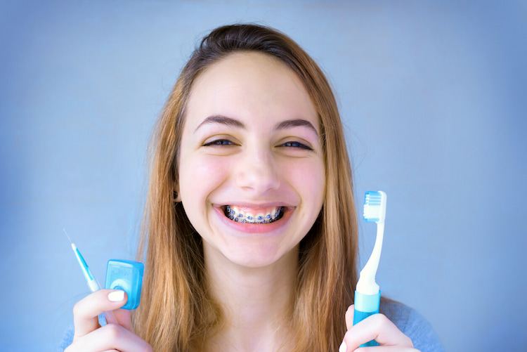 a photo of a young lady holding a tooth brush and floss to show how to keep your braces clean